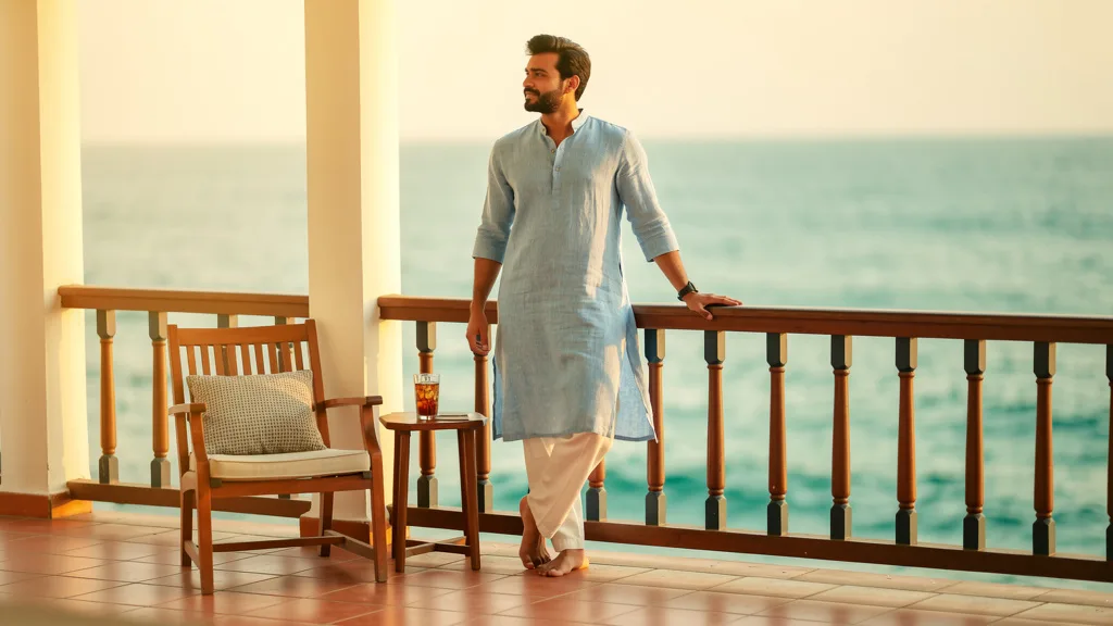 Click to manage / replace image Man wearing a light blue linen kurta looking relaxed on a beachside balcony.